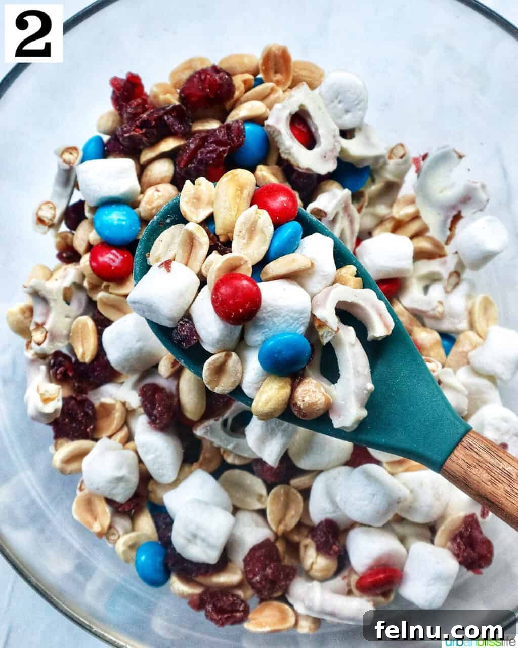 Stars and Stripes Snack Blend 6 A spoon lifting a scoop of mixed red, white, and blue trail mix over a full bowl, demonstrating the final product.