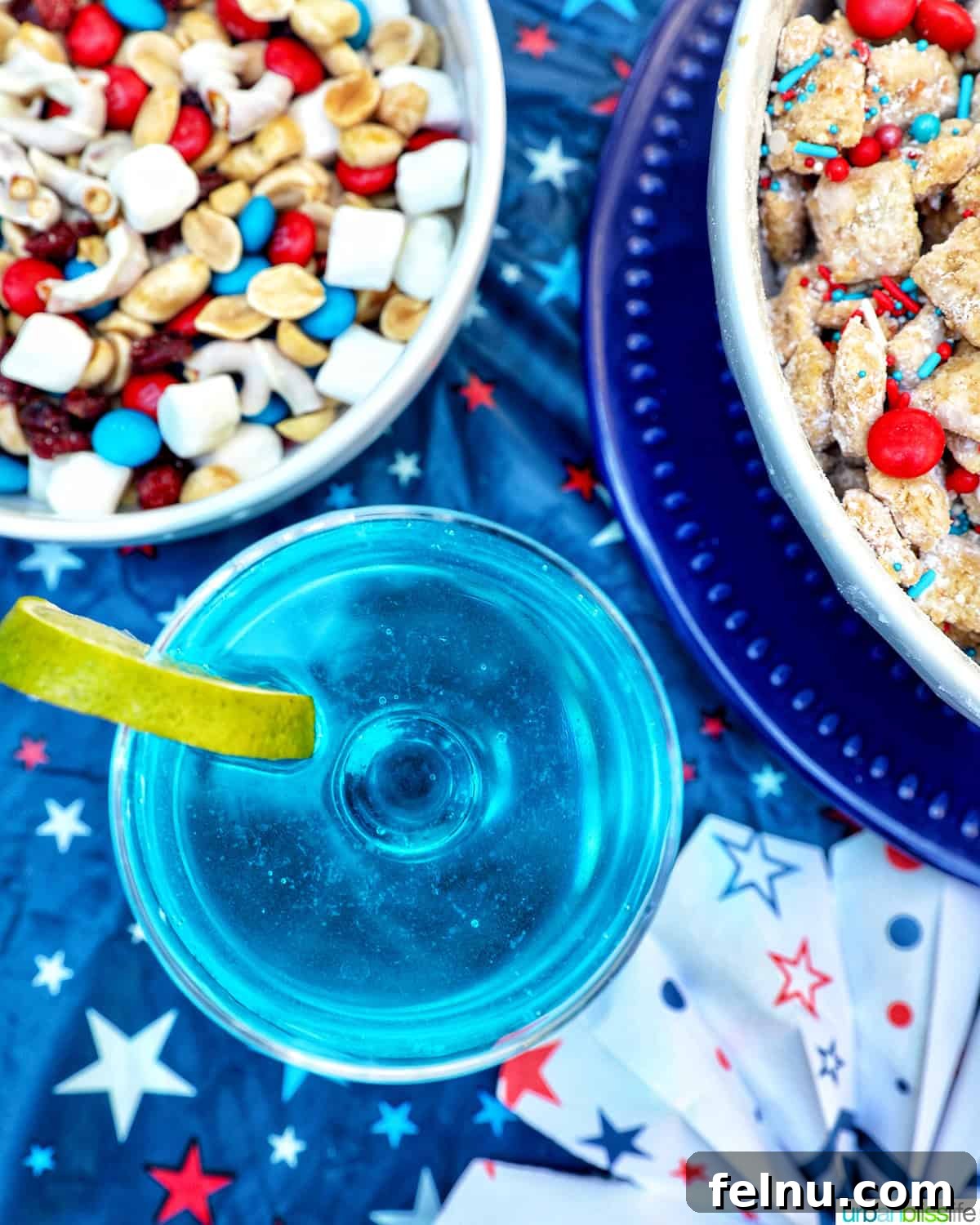 Stars and Stripes Snack Blend 9 Overhead view of a vibrant blue wave cocktail surrounded by bowls of red, white, and blue puppy chow and trail mix.