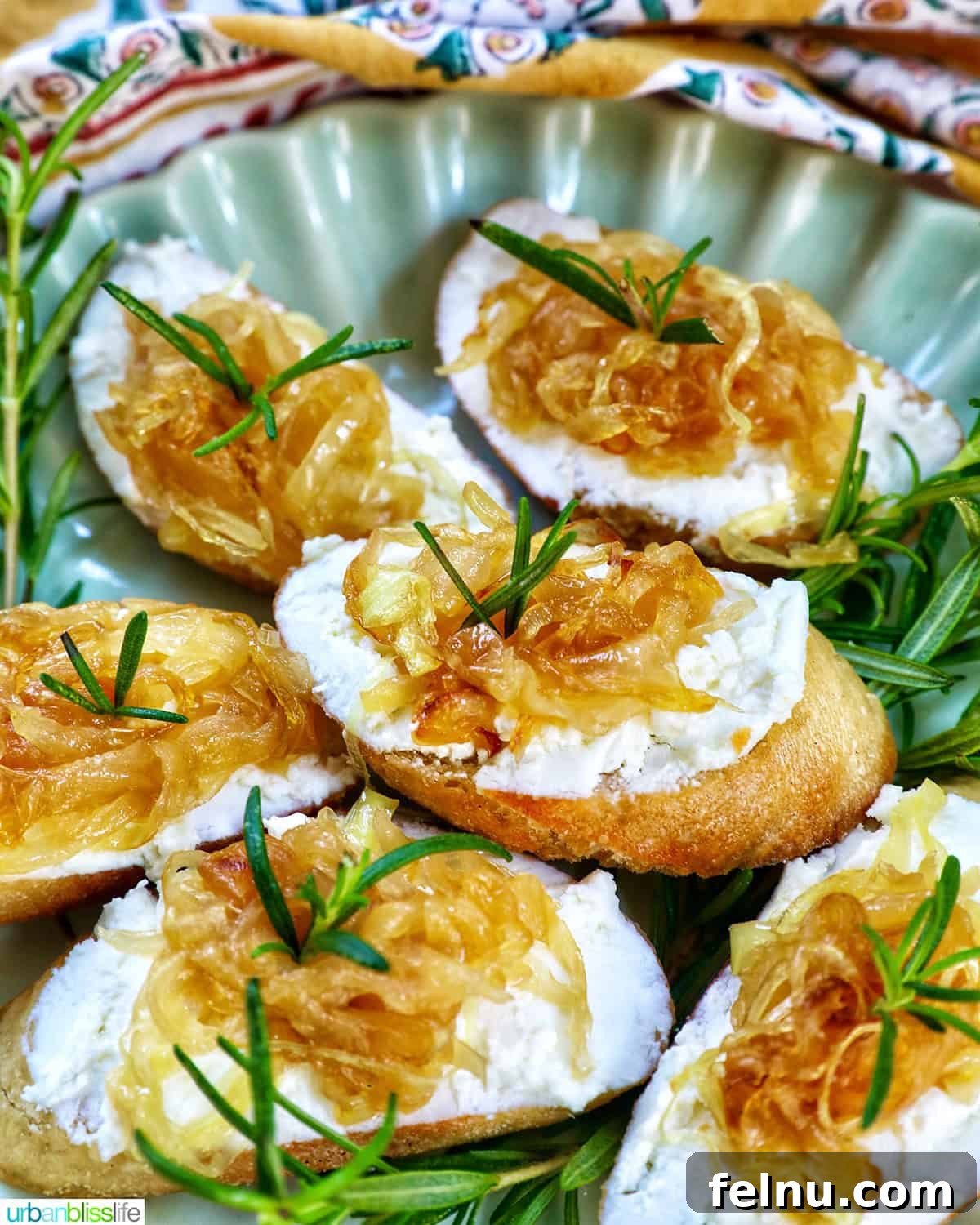 Golden Onion and Chevre Morsels 2 Caramelized onion and goat cheese crostini on a plate, garnished with a rosemary sprig, ready to be served.