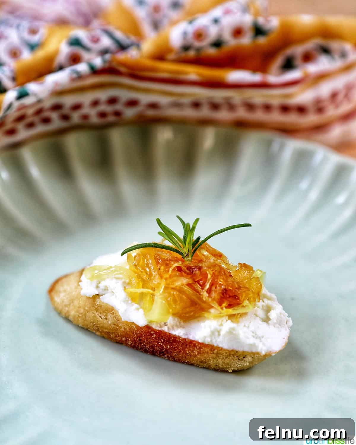 Golden Onion and Chevre Morsels 11 A single caramelized onion and goat cheese crostini on a plate, garnished with a sprig of rosemary.