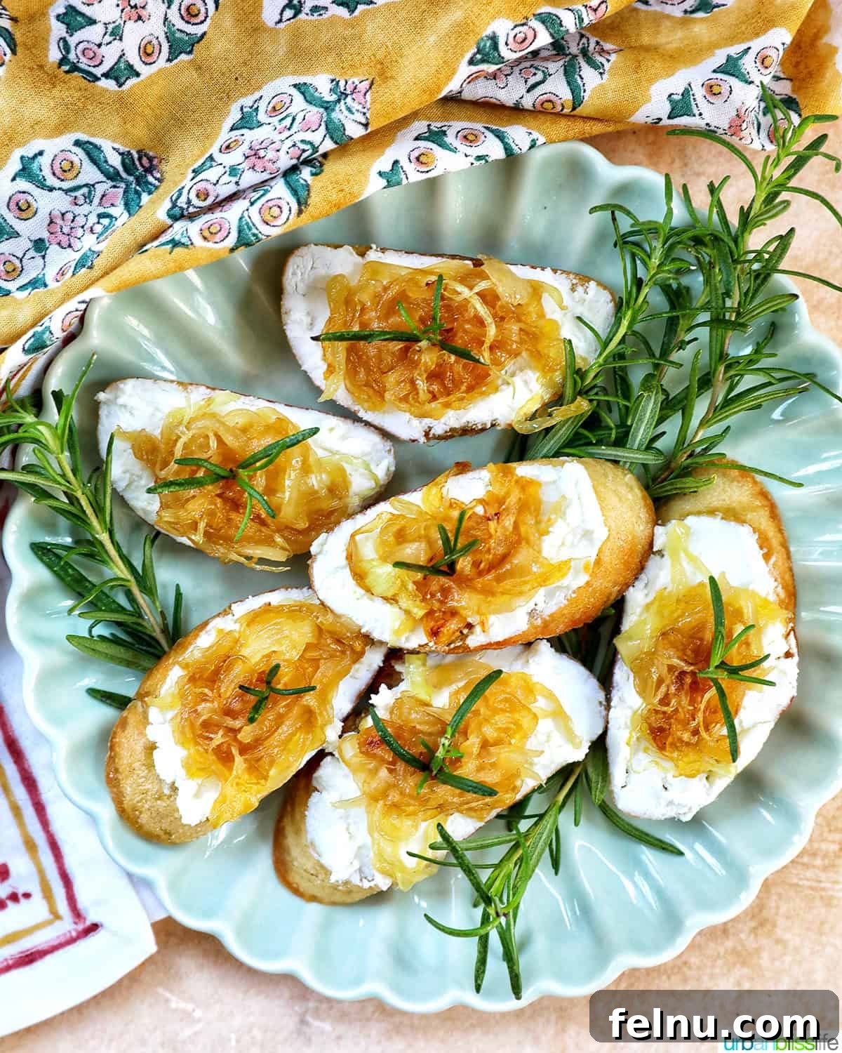 Golden Onion and Chevre Morsels 3 Overhead view of several caramelized onion and goat cheese crostini artfully arranged on a plate with fresh rosemary garnish.