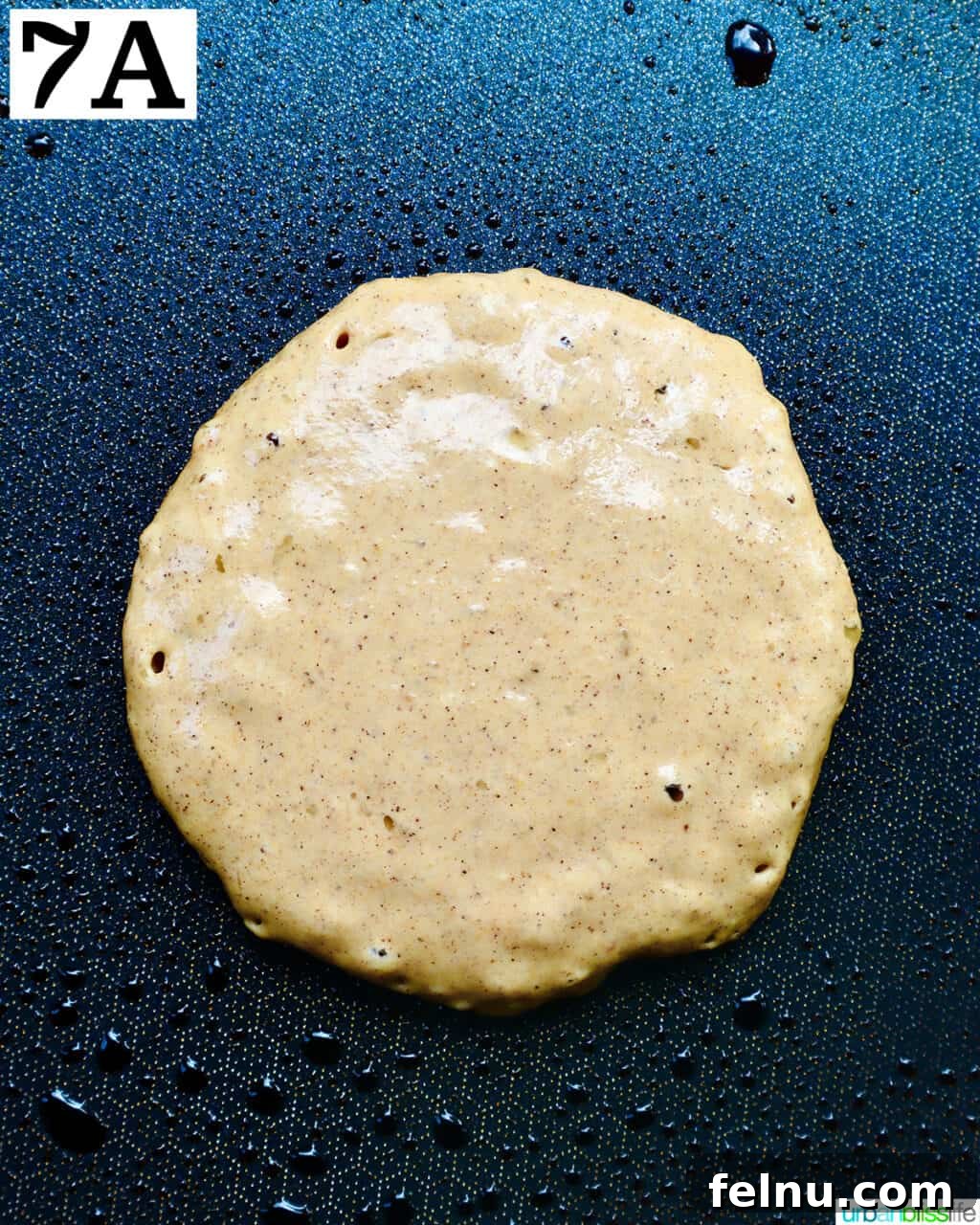 Pancake cooking on a griddle, with bubbles forming.