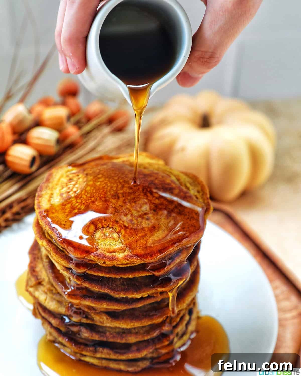 Stack of pumpkin spice pancakes on a plate with someone pouring maple syrup.