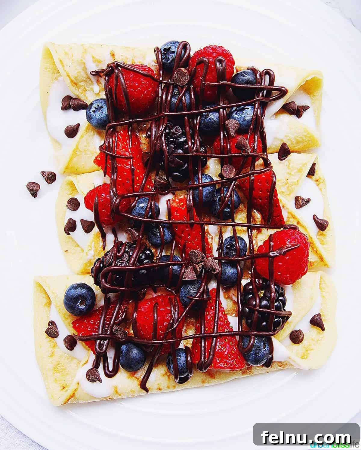 Iconic French Culinary Delights 14 Delicate crêpes artfully folded and topped with a vibrant medley of mixed berries and a decadent drizzle of chocolate sauce.