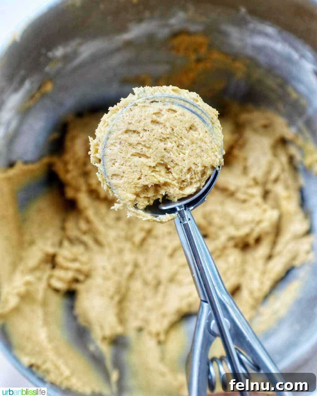 cookie scoop with pumpkin pie spice cookie batter in it above a bowl of batter.
