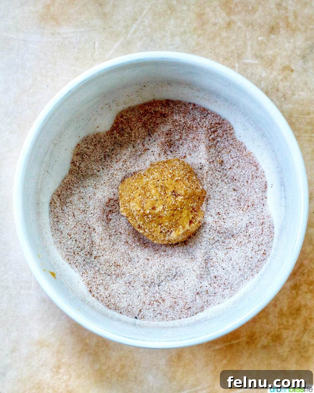 pumpkin pie spice cookie dough ball rolling in cinnamon sugar.