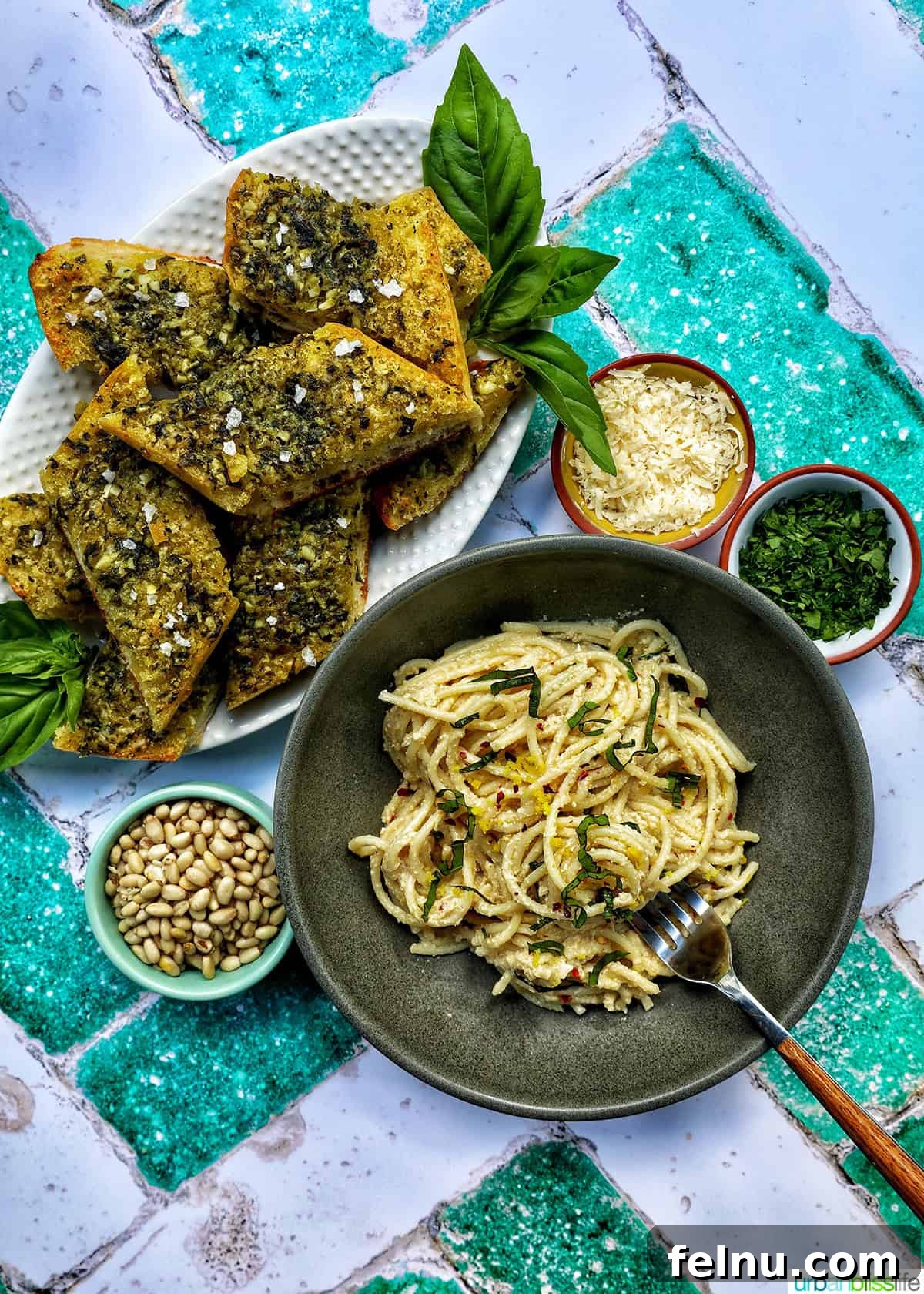 Effortless Weeknight Meals 4 Slices of pesto bread on a white platter with glass of white wine and bowl of tahini pasta, with bowls of garnishes.