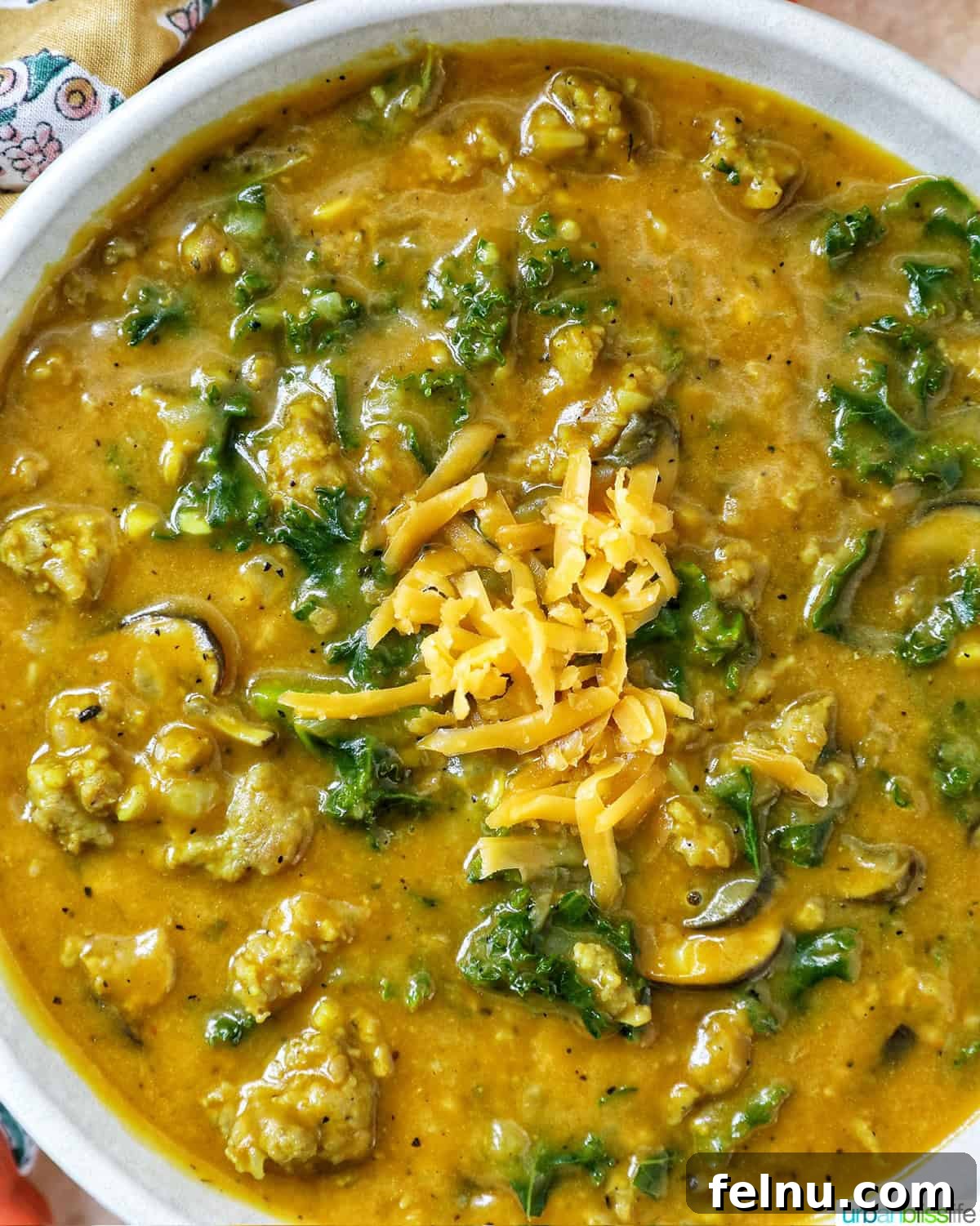 Smoky Sausage Pumpkin Bisque 2 A vibrant bowl of pumpkin soup with sausage, garnished with fresh greens and a sprinkle of cheese, evoking warmth and comfort.