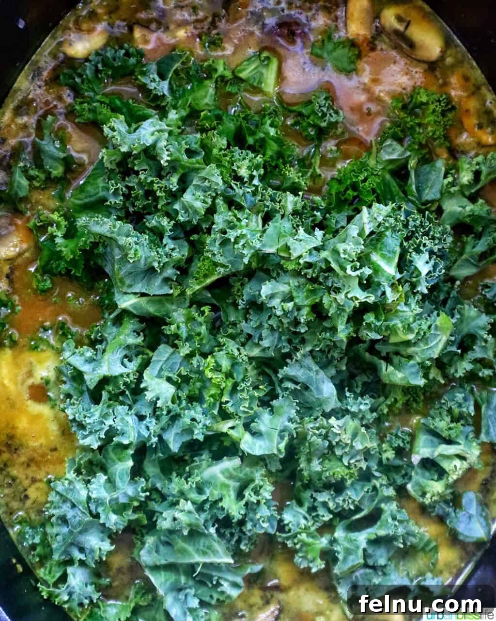 Smoky Sausage Pumpkin Bisque 12 Fresh, vibrant chopped kale being stirred into the pumpkin sausage soup in a pot, adding a healthy and colorful finish.