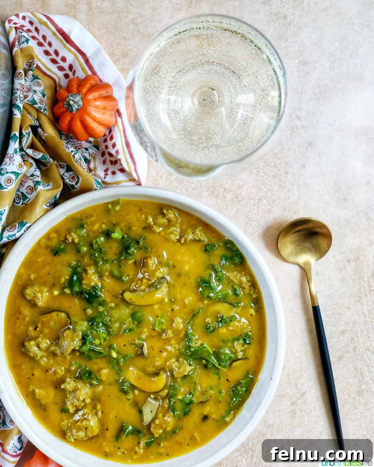 Smoky Sausage Pumpkin Bisque 17 An inviting overhead view of a bowl of pumpkin soup with sausage, artfully placed next to a spoon and a glass of complementary white wine, suggesting a delightful meal.