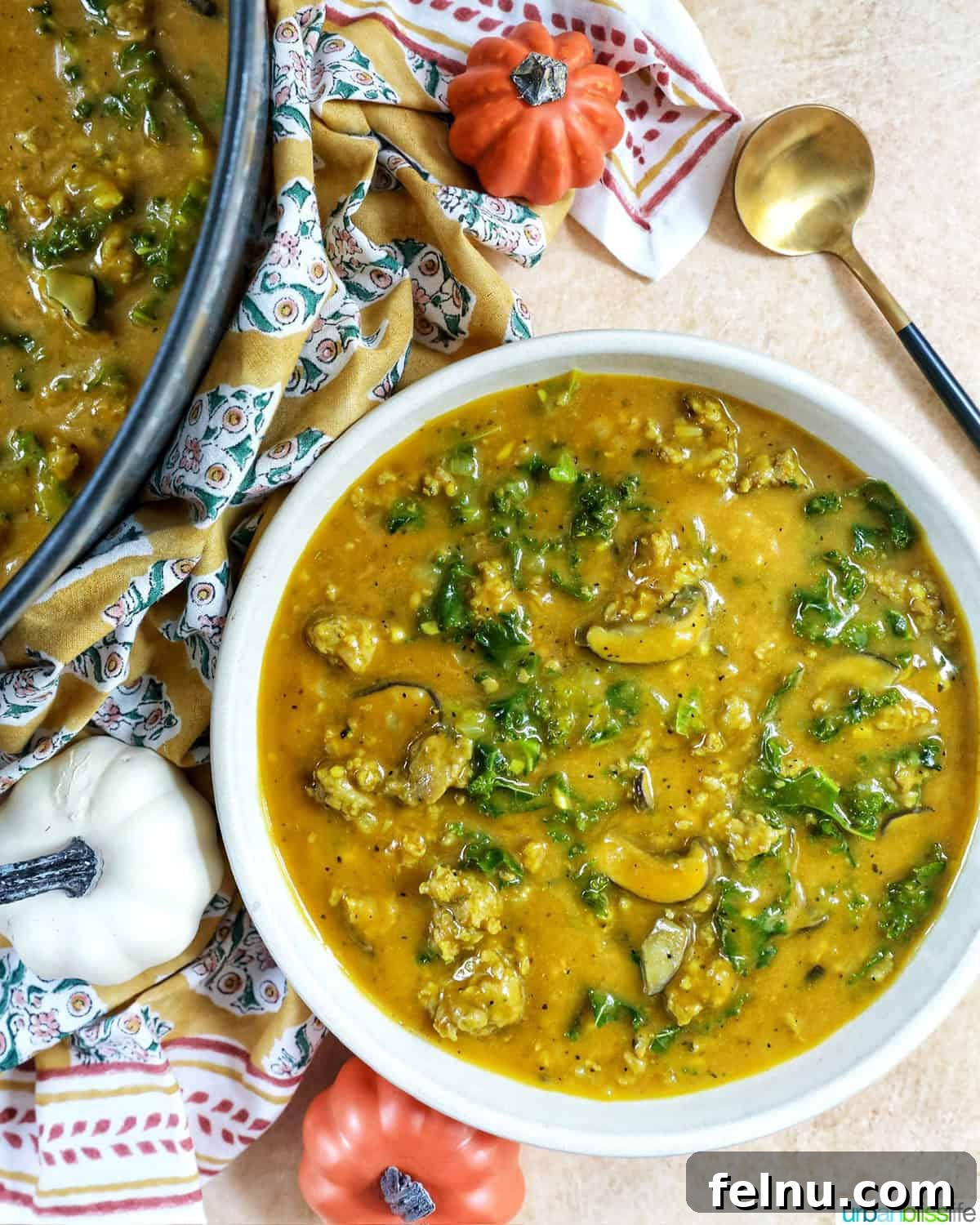 Smoky Sausage Pumpkin Bisque 18 An overhead shot of a prepared bowl of pumpkin soup with sausage, a large Dutch oven filled with soup, a stirring spoon, and decorative mini pumpkins, showcasing a complete and inviting setup.
