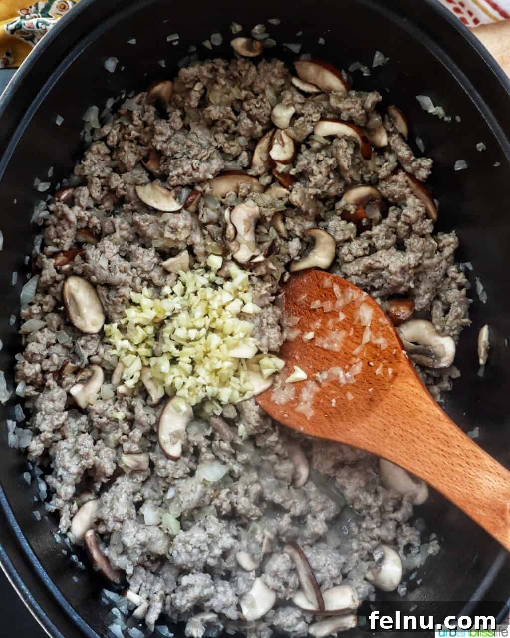 Smoky Sausage Pumpkin Bisque 7 A wooden spoon gently mixing fragrant ginger with browned ground meat and sautéed mushrooms in a Dutch oven, infusing the base with warm spices.