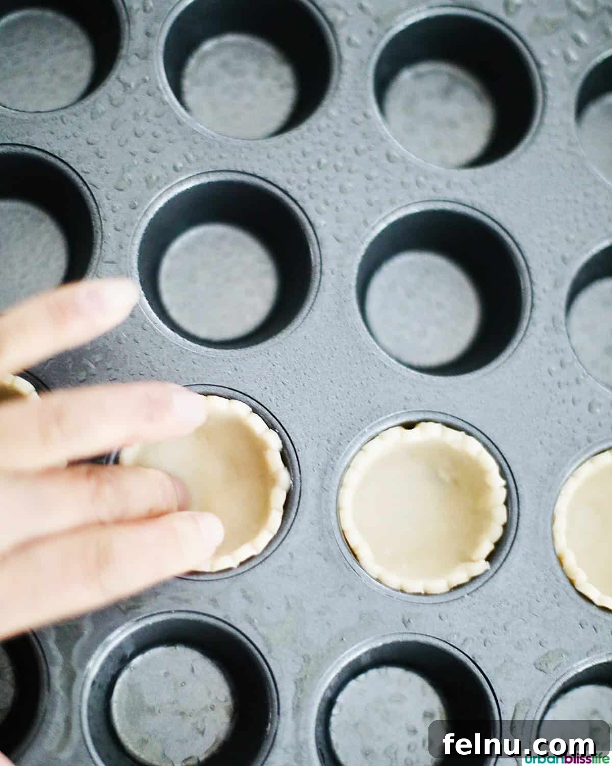 Mini Pecan Tarts 8 Hand pressing pie crust dough into a mini muffin tin.