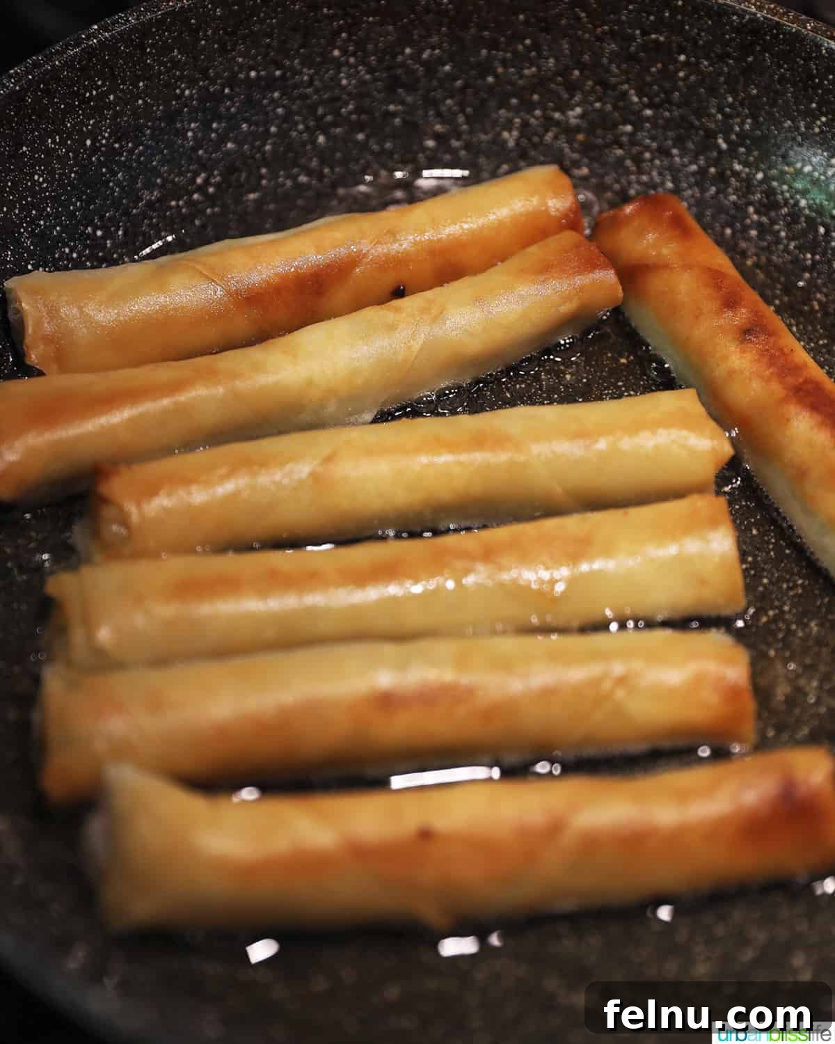 Filipino lumpia frying in hot oil in a skillet, turning golden brown and crispy.