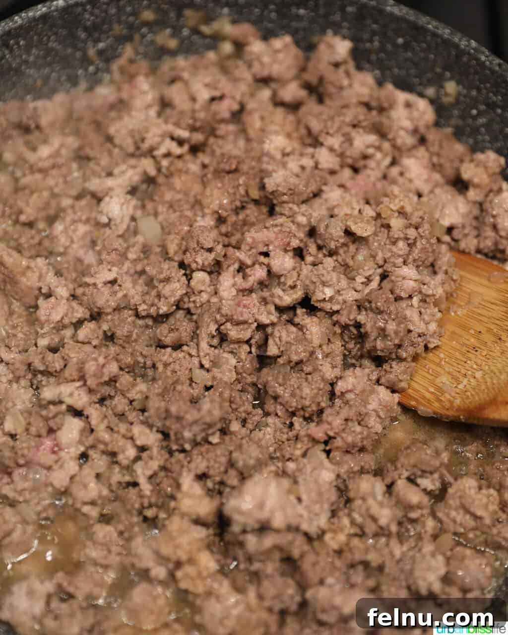 Ground meat browning in a skillet, stirred with a wooden spoon, forming the base of the lumpia filling.