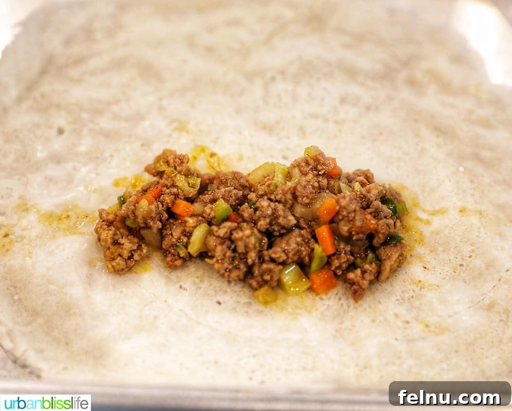 A generous tablespoon of savory lumpia filling placed diagonally on a thin lumpia wrapper, ready for folding.