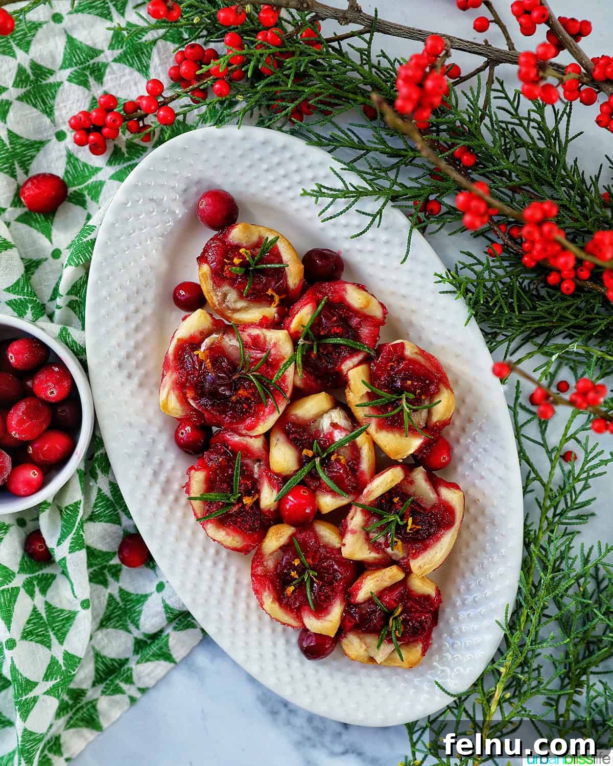 Cranberry brie tartlet appetizers on a plate next to a plate of pistachio cranberry shortbread cookies and glasses of cranberry mocktails with holiday decor.