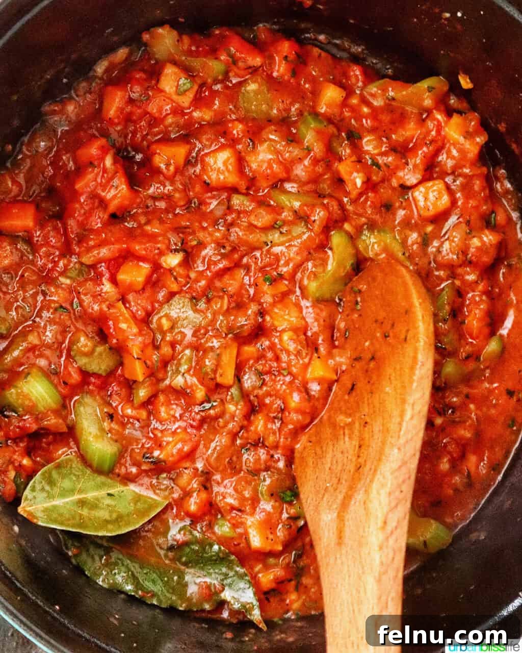wooden spoon stirring sauce in a Dutch oven.