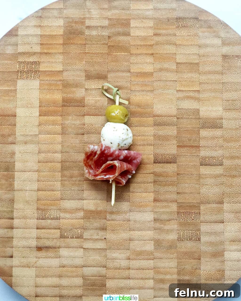 Antipasto Holiday Wreath 10 Food pick with an olive, mozzarella ball, and salami on a cutting board