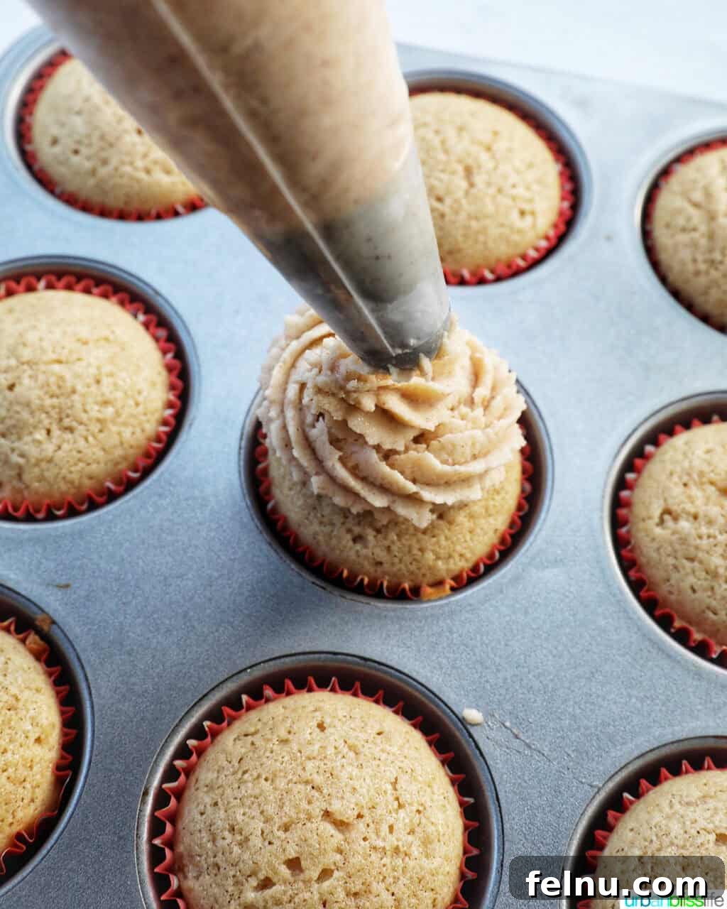 Cinnamon Swirl Delights 19 Piping bag piping cinnamon frosting onto cupcakes.