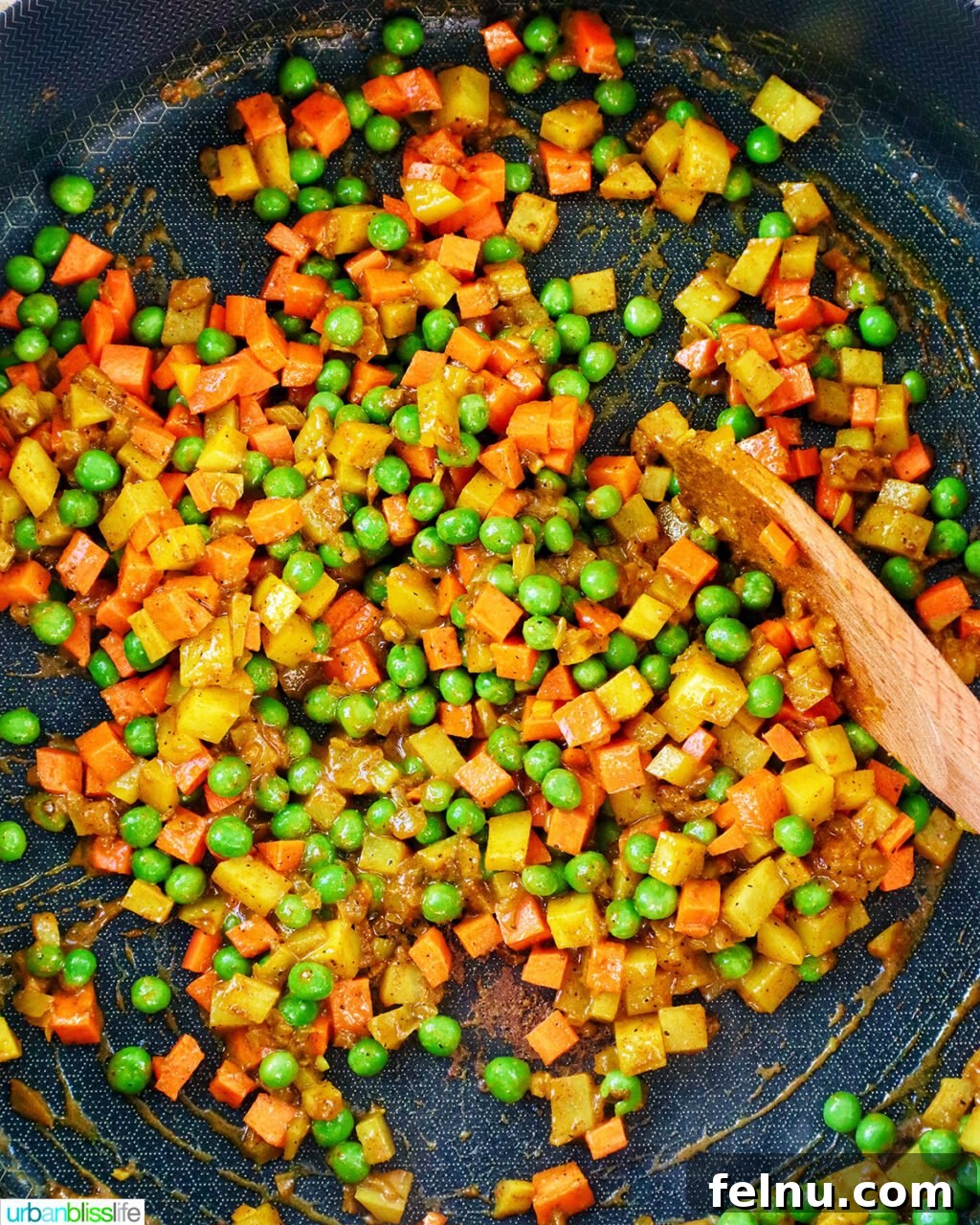 Peas, carrots added to potatoes and curry spices in a pan.