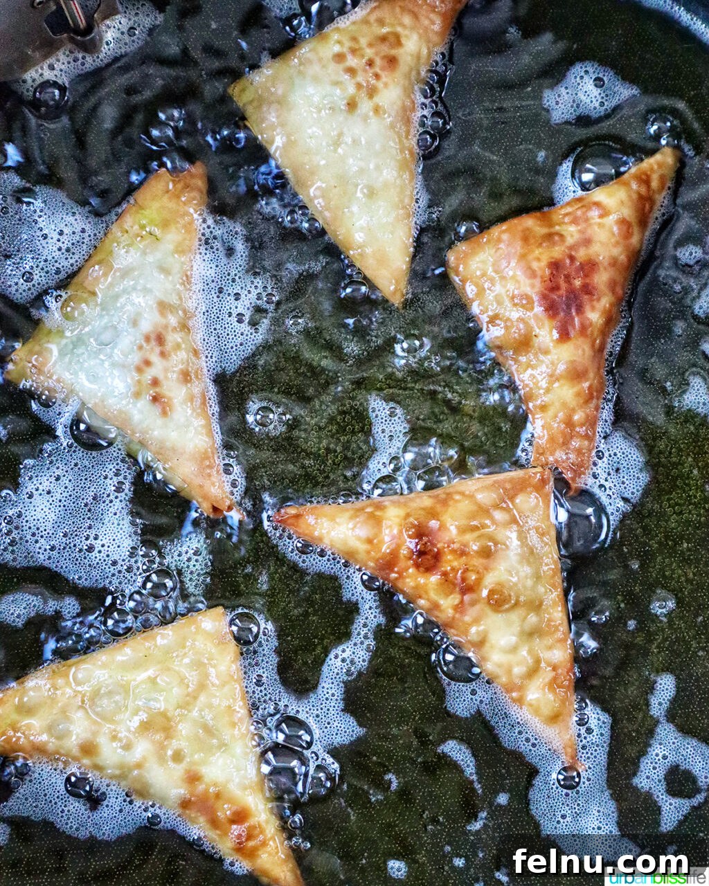 Vegan curry samosas frying in a Dutch oven.