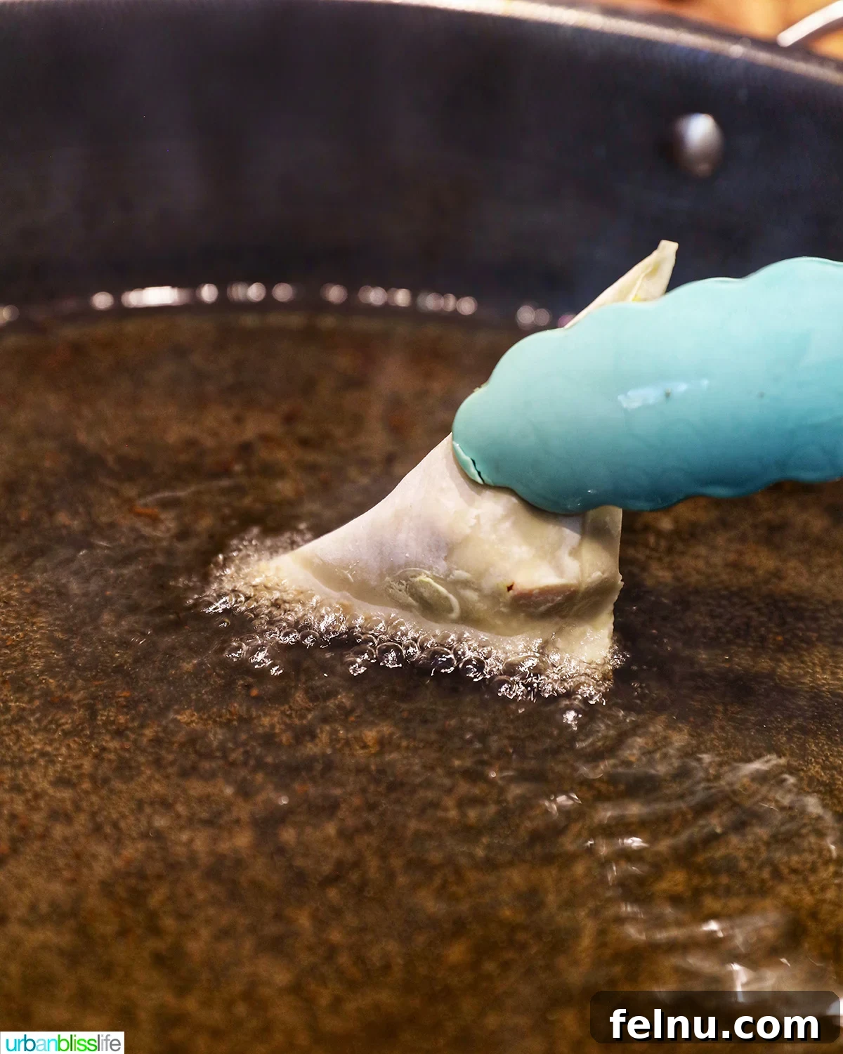 Tongs dipping one side of a samosa into hot oil.