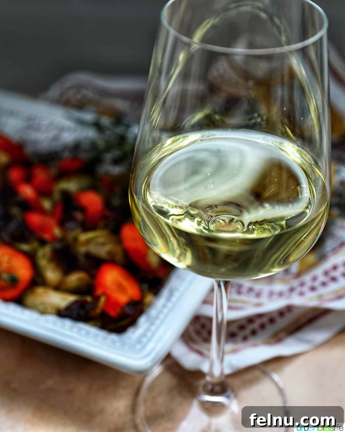 Roasted brussels sprouts and carrot slices in a bowl with a glass of white wine.