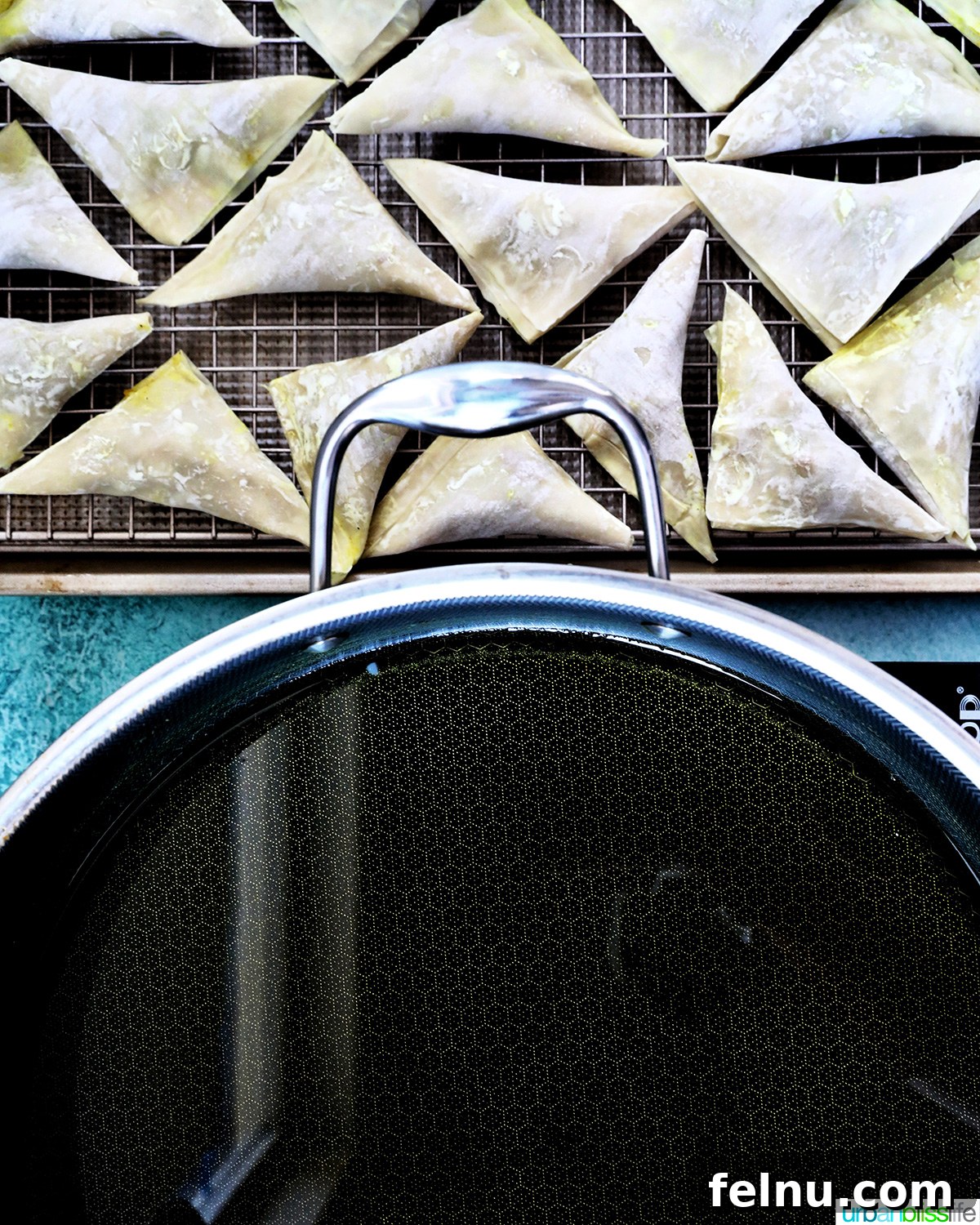 Extra pan of oil and uncooked samosas on a rack.