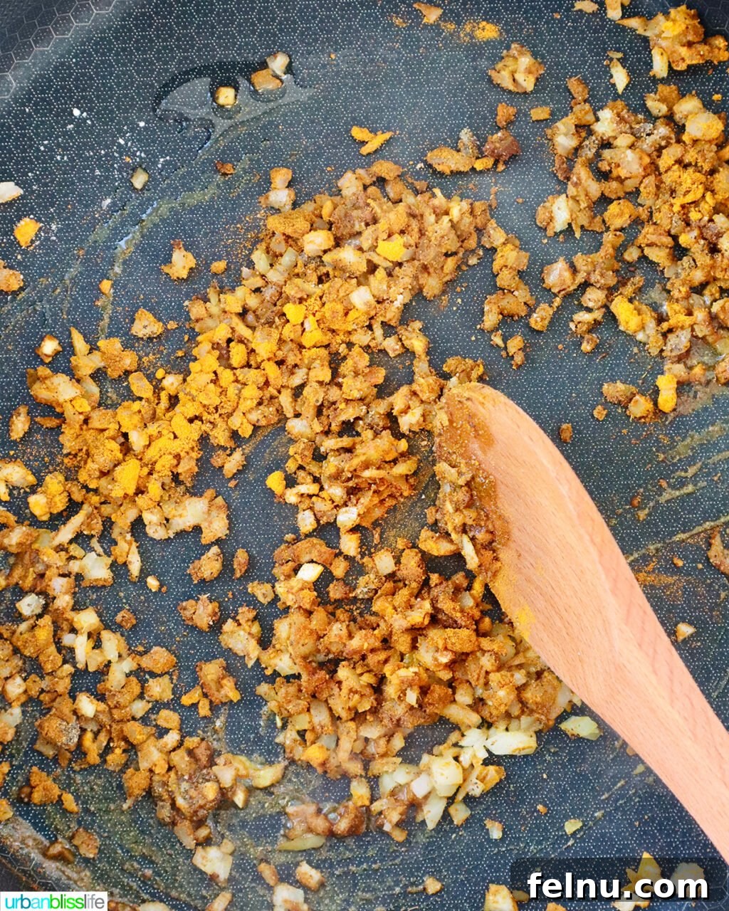 Wooden spoon stirring curry spices and garlic in a pan.