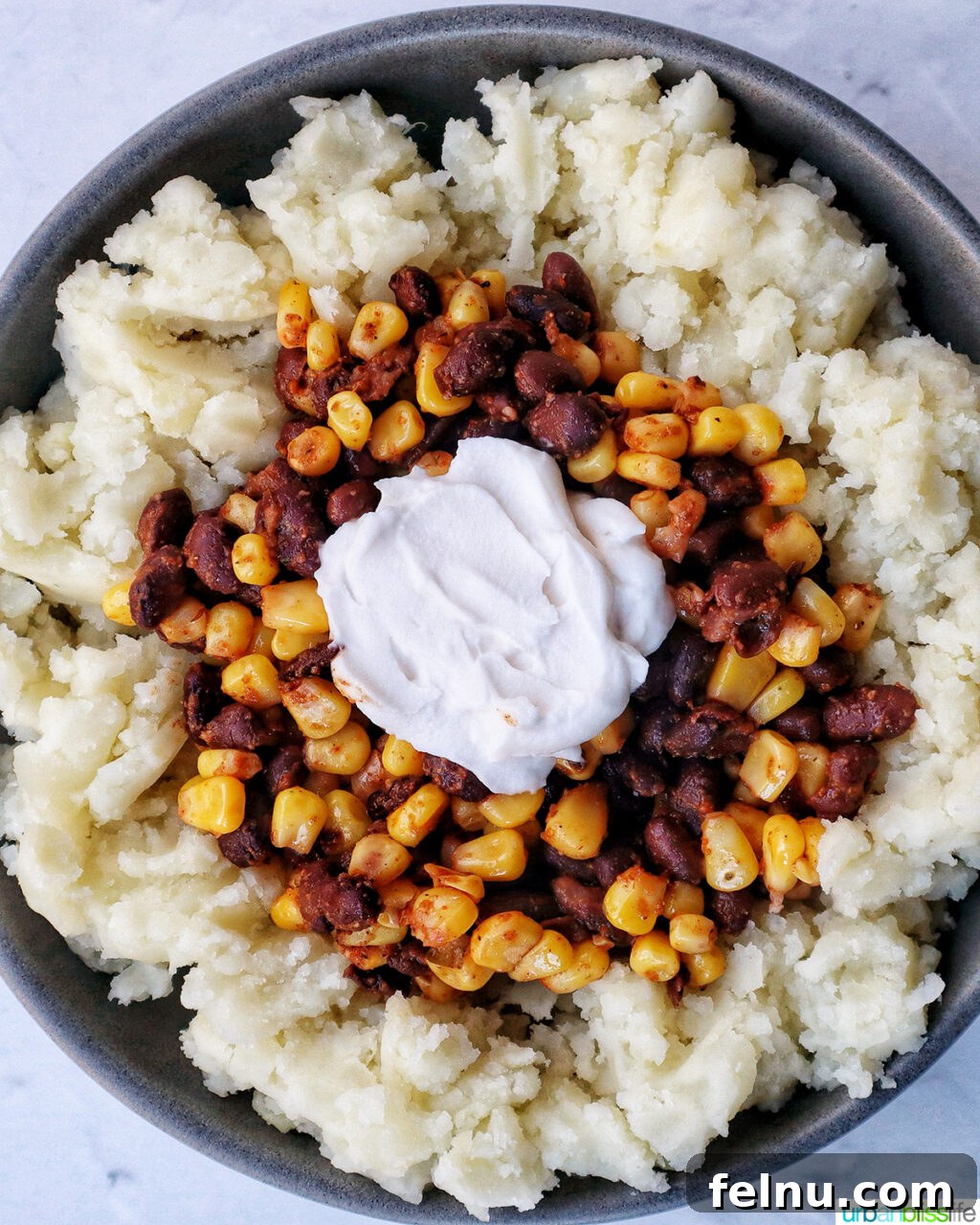 Hearty Spud Indulgence 13 A loaded potato bowl with mashed potatoes, corn, beans, and a dollop of sour cream on top.