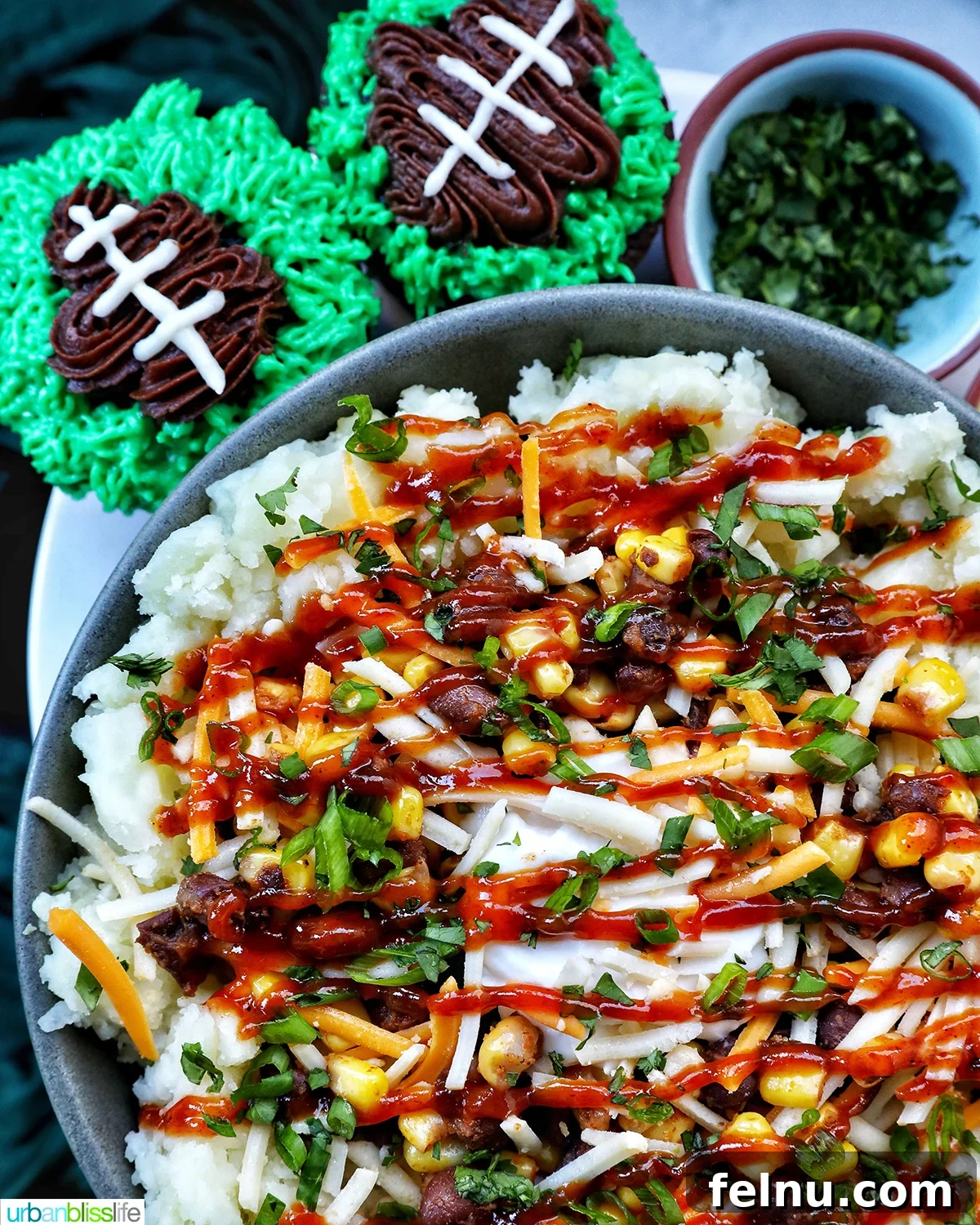 Hearty Spud Indulgence 19 A loaded potato bowl with mashed potatoes, beans, corn, cheese, and herbs, served alongside festive football-themed cupcakes, perfect for Game Day.