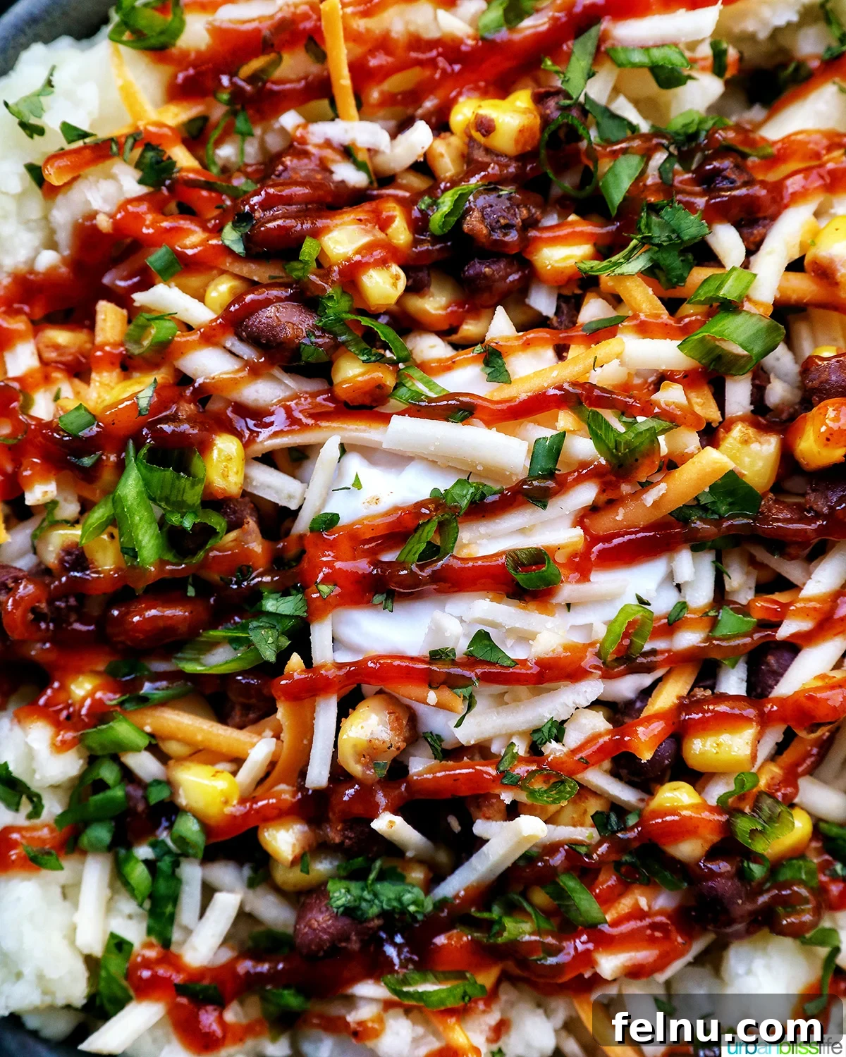 Hearty Spud Indulgence 3 Close-up of a loaded potato bowl showcasing fluffy mashed potatoes, seasoned black beans, sweet corn kernels, a generous sprinkle of golden shredded cheese, and fresh green herbs.