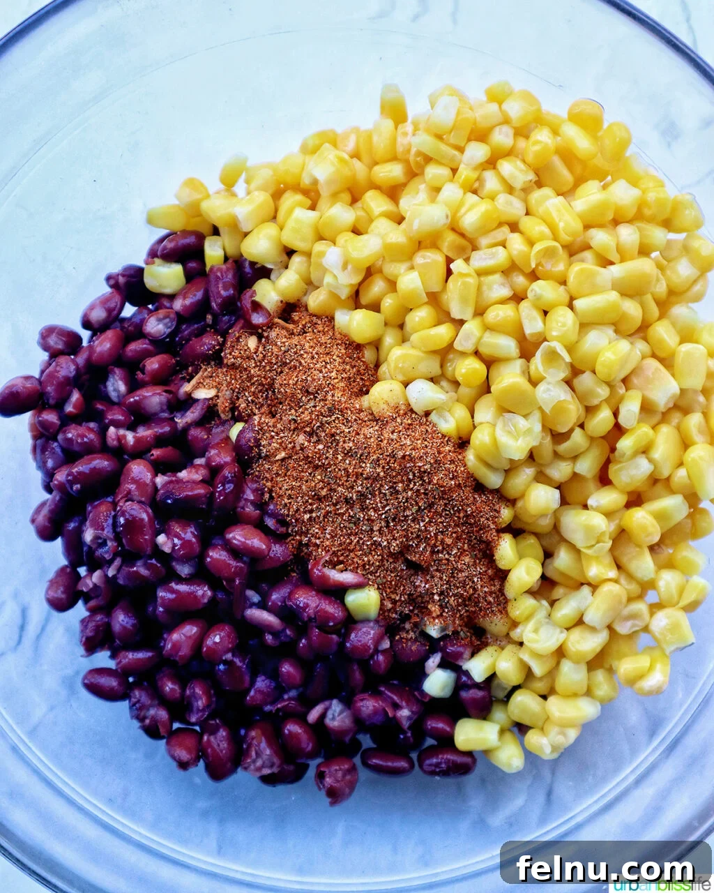 Hearty Spud Indulgence 6 A bowl filled with frozen corn kernels, black beans, and taco seasoning, ready to be mixed.
