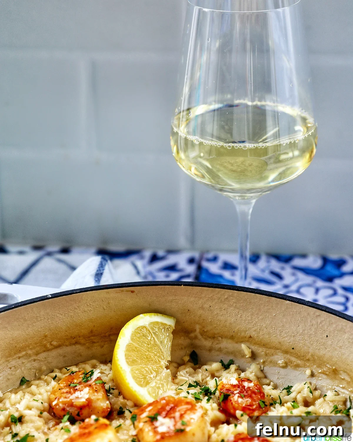 The Art of Pairing Wine with Scallops 4 braising pan with scallop risotto with lemon wedge and parsley garnish with glass of white wine.