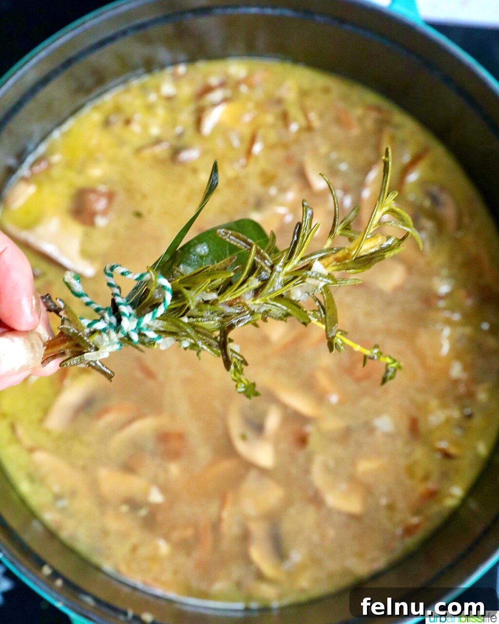 Creamy Vegan Mushroom Delight 14 A bouquet of fresh herbs being removed from a pot of dairy free mushroom soup.
