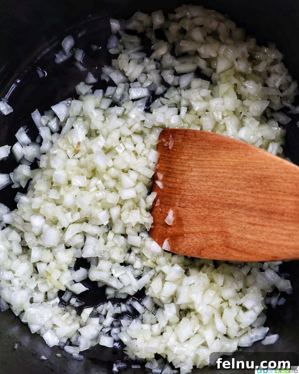 Creamy Vegan Mushroom Delight 6 Finely diced onions being added to a Dutch oven with a wooden spoon.