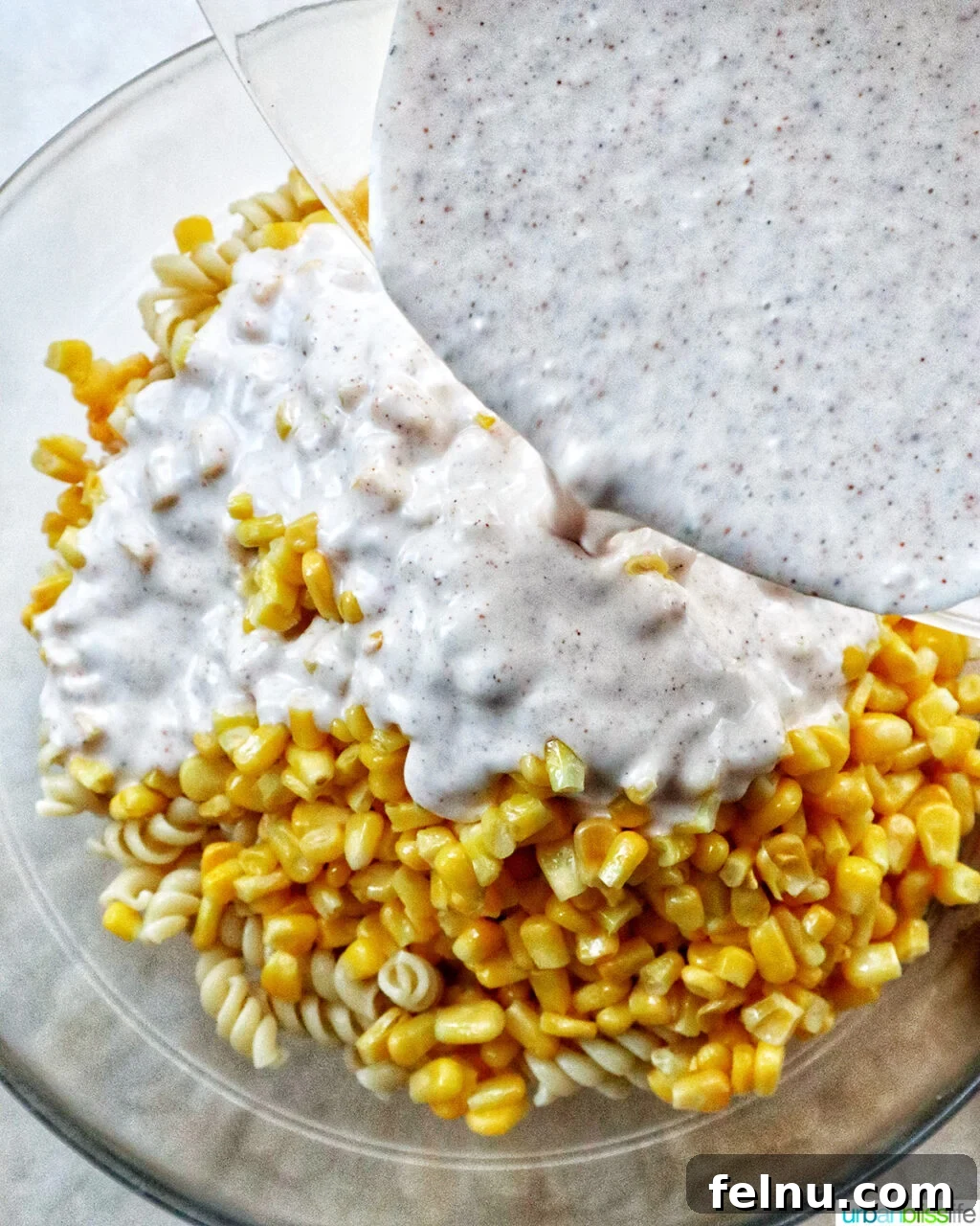 Zesty Elote Pasta Salad 11 Pasta and corn being gently tossed with the rich, creamy dressing in a spacious mixing bowl.