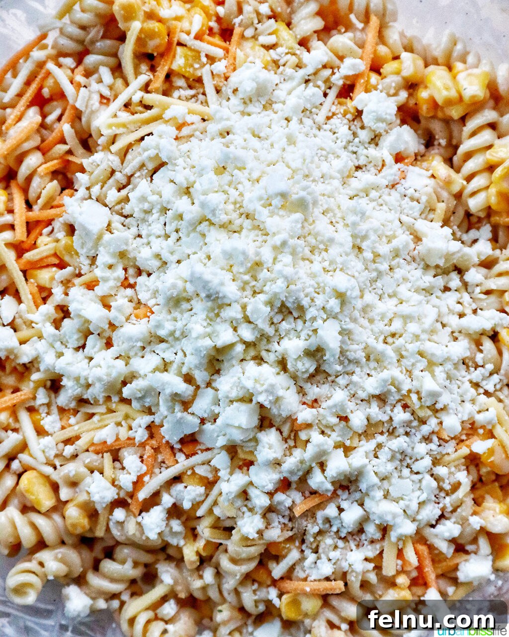 Zesty Elote Pasta Salad 13 Crumbled Cotija cheese being generously added to the Mexican street corn pasta salad, providing a salty, tangy finish.