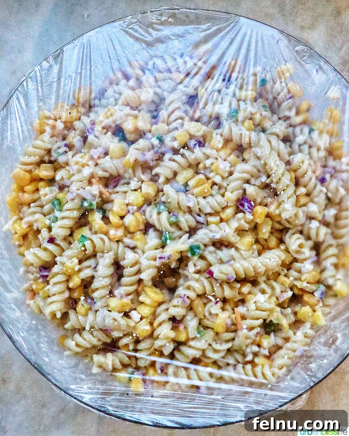 Zesty Elote Pasta Salad 15 A large bowl of Mexican street corn pasta salad, freshly made and covered with plastic wrap, being placed into the refrigerator to chill.