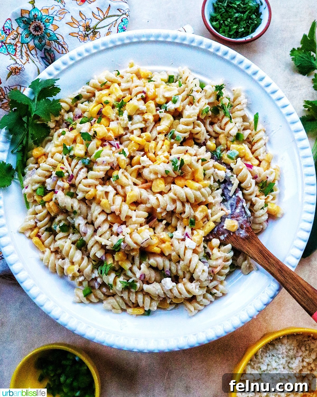 Zesty Elote Pasta Salad 17 Mexican street corn pasta salad elegantly presented in a white bowl with a wooden serving spoon, suggesting it's ready for a sophisticated yet casual meal.