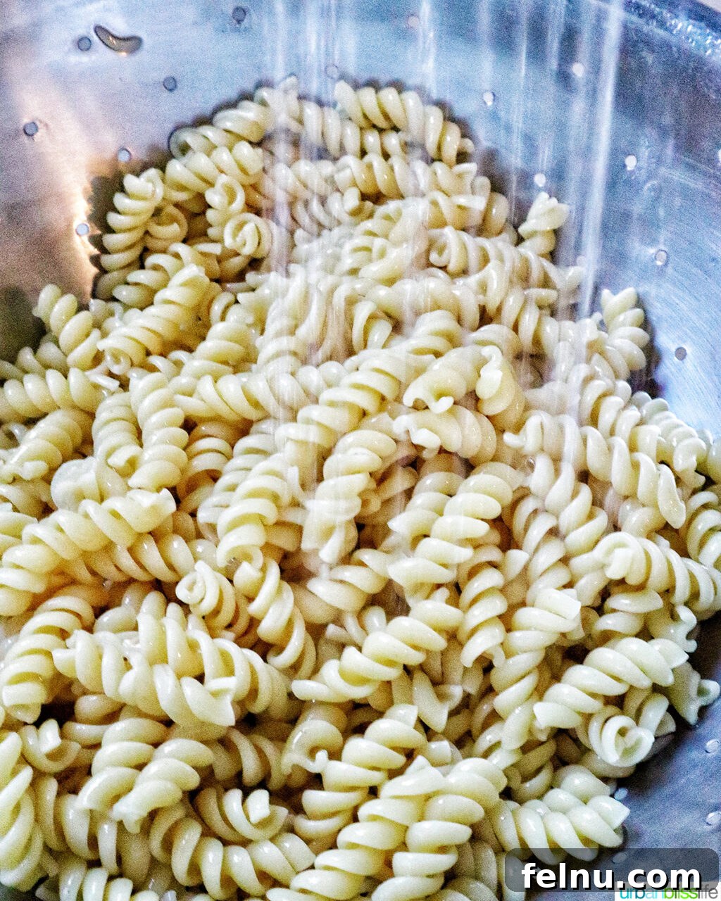 Zesty Elote Pasta Salad 9 Cooked pasta being rinsed under cold running water in a colander to cool it down and prevent sticking.