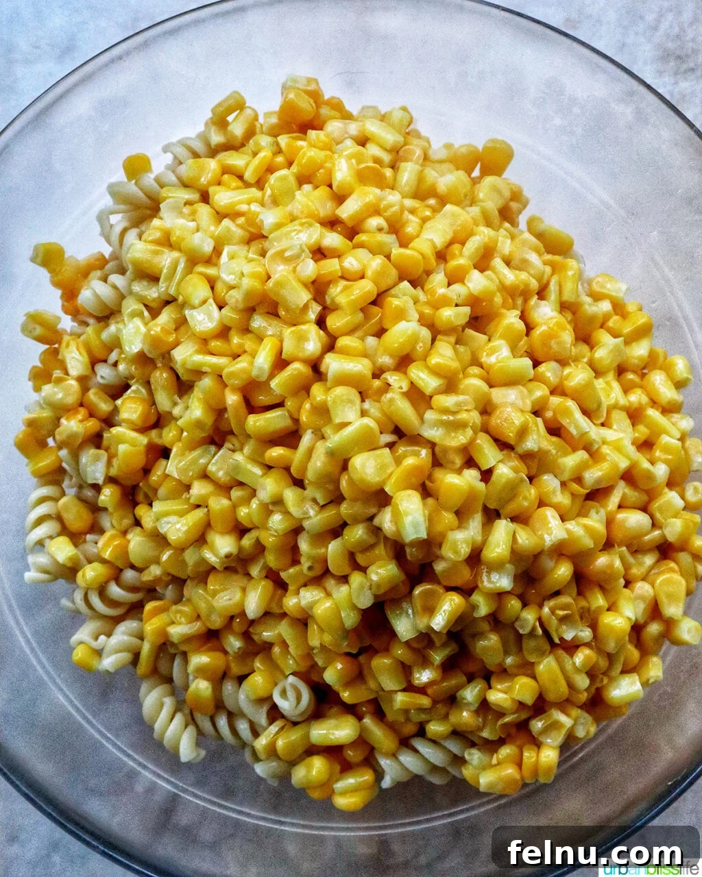 Zesty Elote Pasta Salad 10 A large mixing bowl containing freshly cooked pasta and bright yellow corn kernels, ready for dressing.