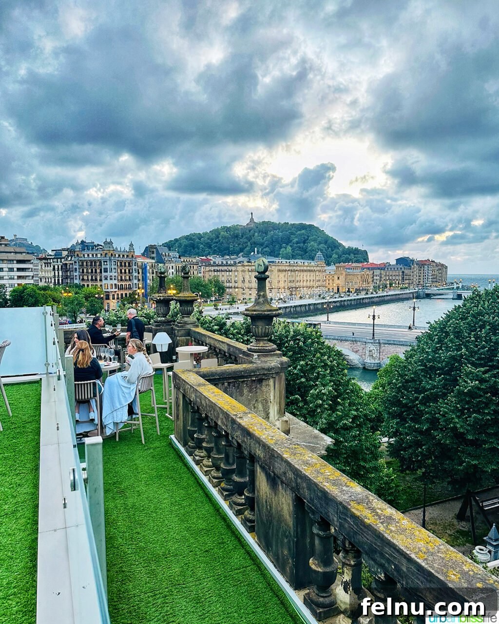 A vibrant rooftop bar scene at Hotel Abba San Sebastian, offering stunning panoramic views of the cityscape and river.