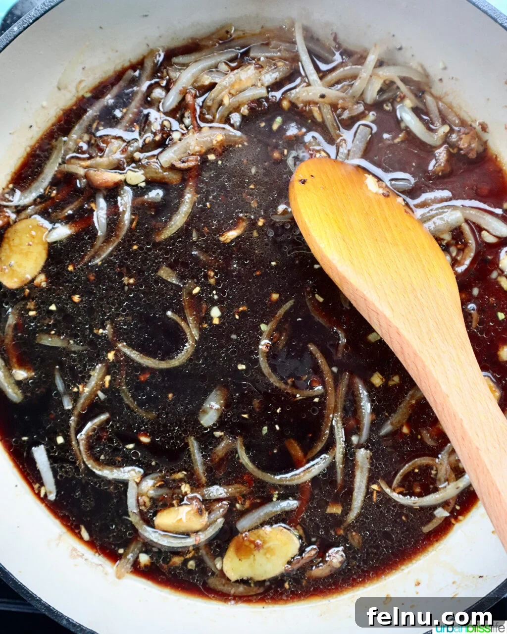 Fragrant Chinese Braised Chicken 11 Wooden spoon stirring the braising sauce into aromatics in a skillet.