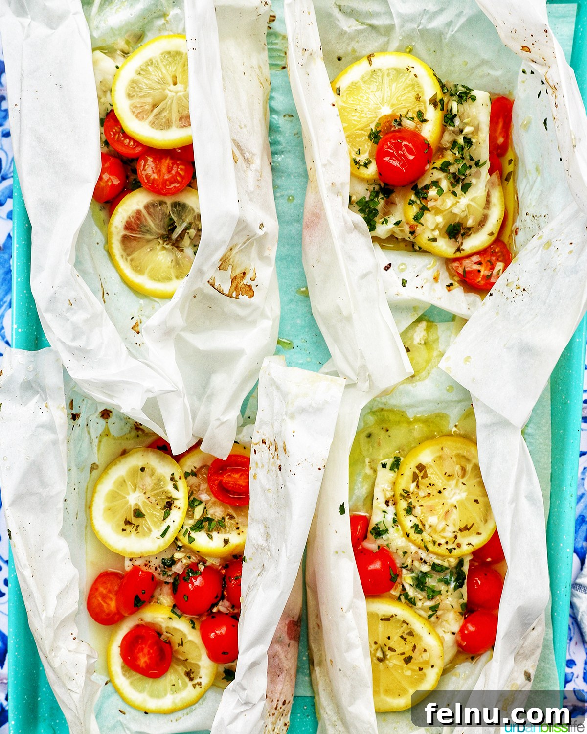 Flaky Cod En Papillote 14 Four perfectly baked Cod en Papillote packets resting on a blue baking sheet.
