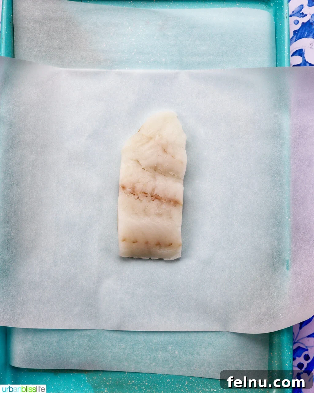 Flaky Cod En Papillote 5 A cod white fish fillet placed on parchment paper on a baking sheet, ready for seasoning.