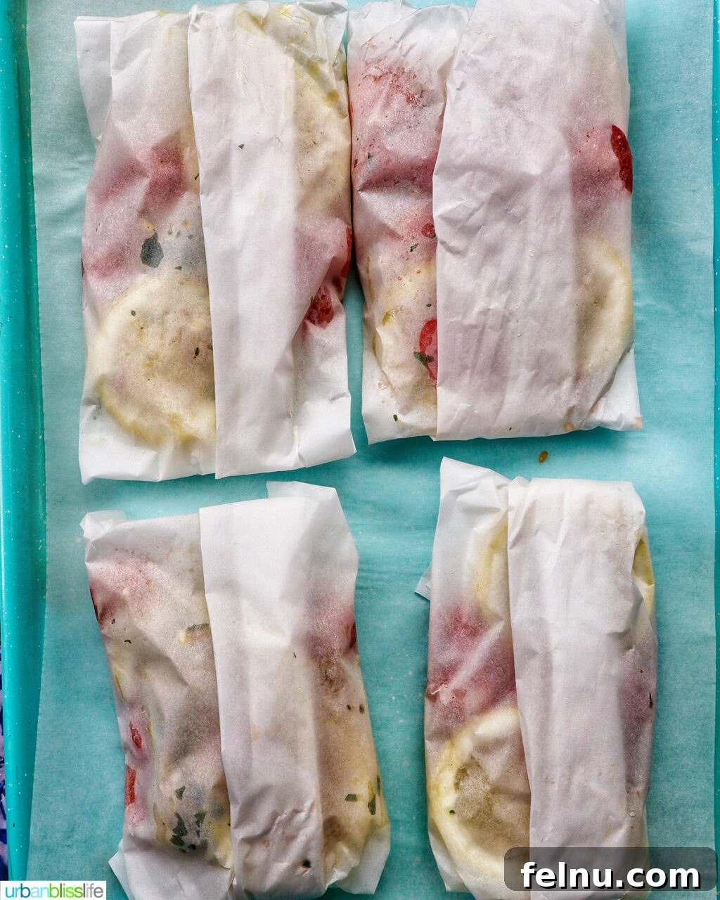 Flaky Cod En Papillote 10 Four beautifully wrapped Cod en Papillote packets arranged on a blue baking sheet, ready for the oven.