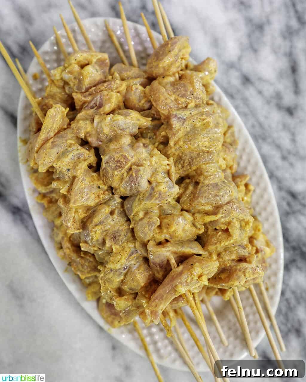 Tandoori Chicken Kebabs 10 Tandoori chicken skewers uncooked on a plate.