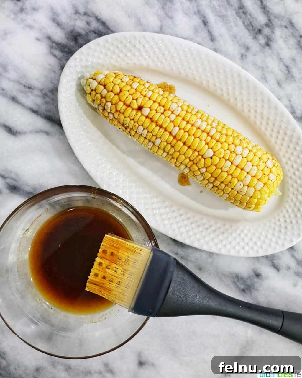 Fire-Kissed Corn Salad 6 Basting brush applying olive oil spice mixture onto corn on the cob.
